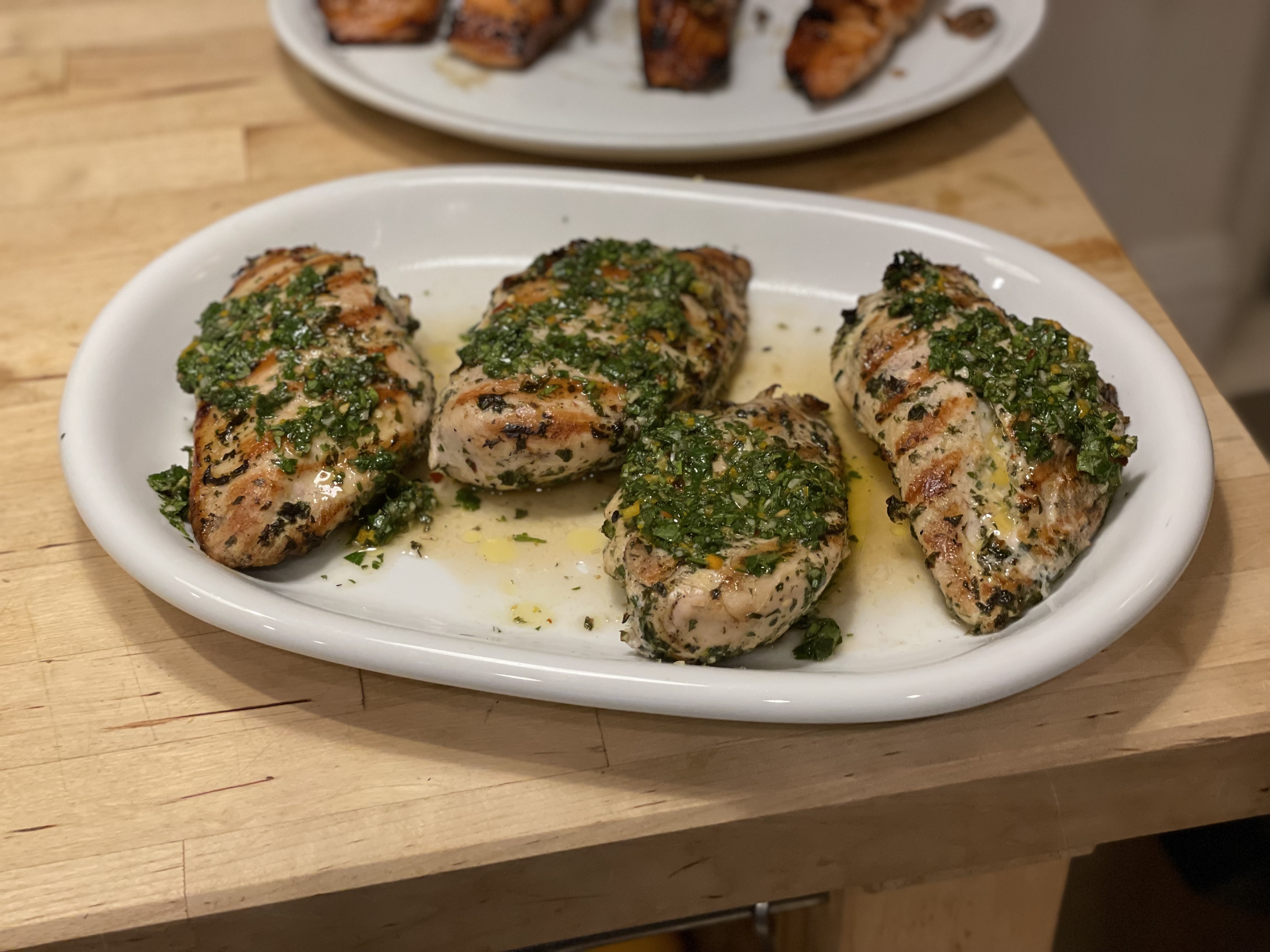 Grilled chicken breasts with chimichurri sauce on a white oval platter