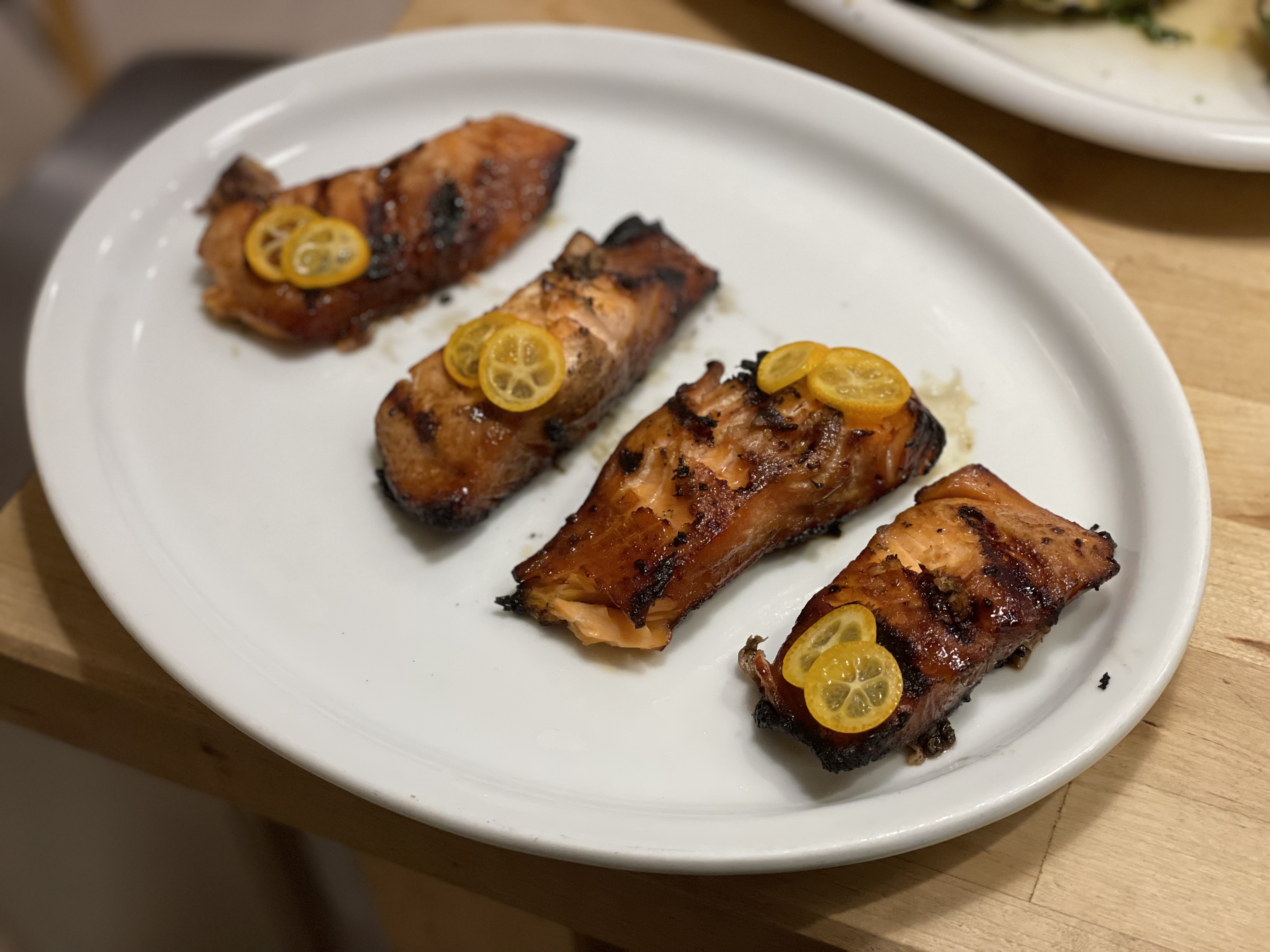 Glazed salmon fillets with kumquat slices on a white oval plate