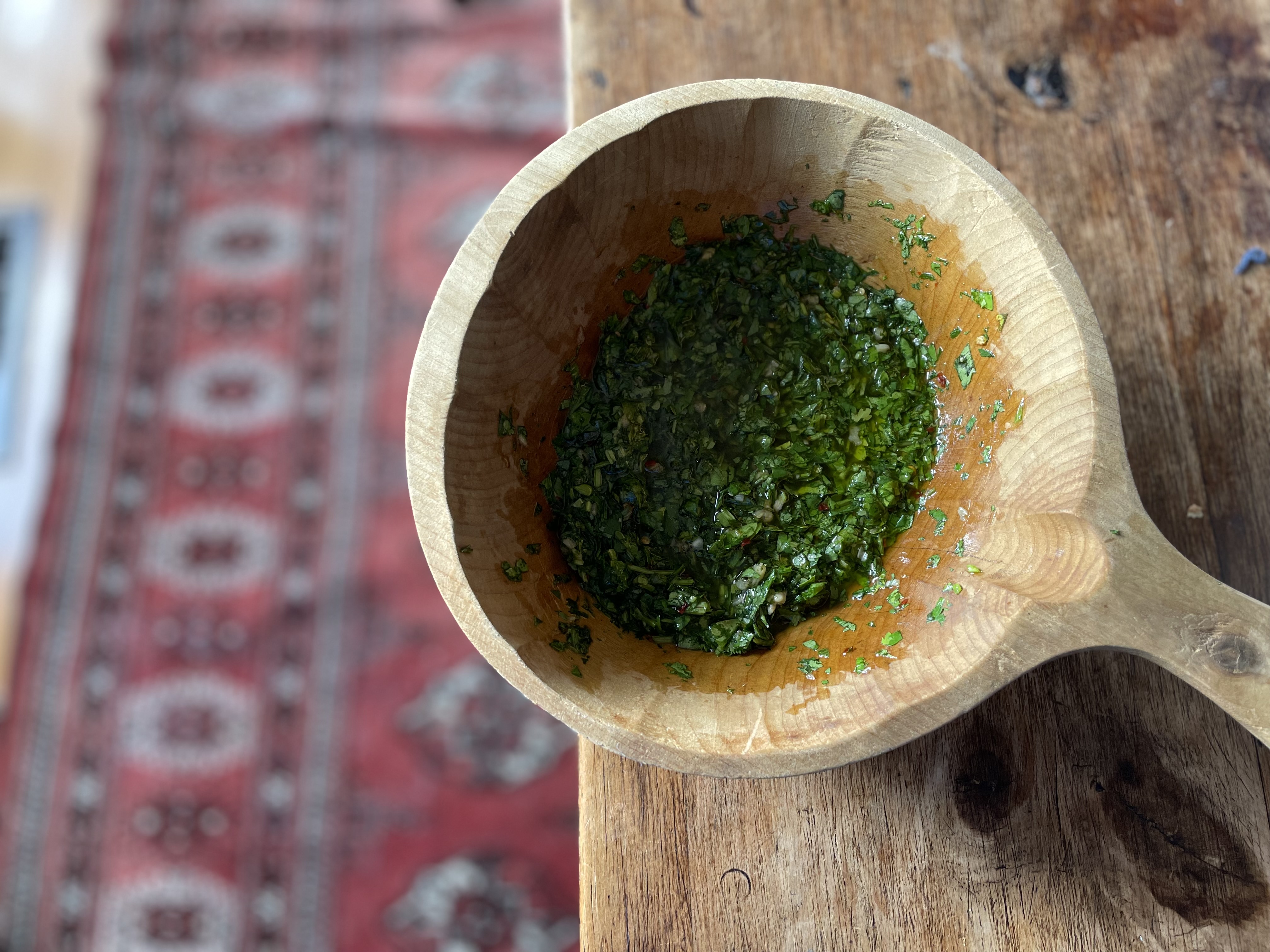 Chopped green herbs in a wooden mortar with oil