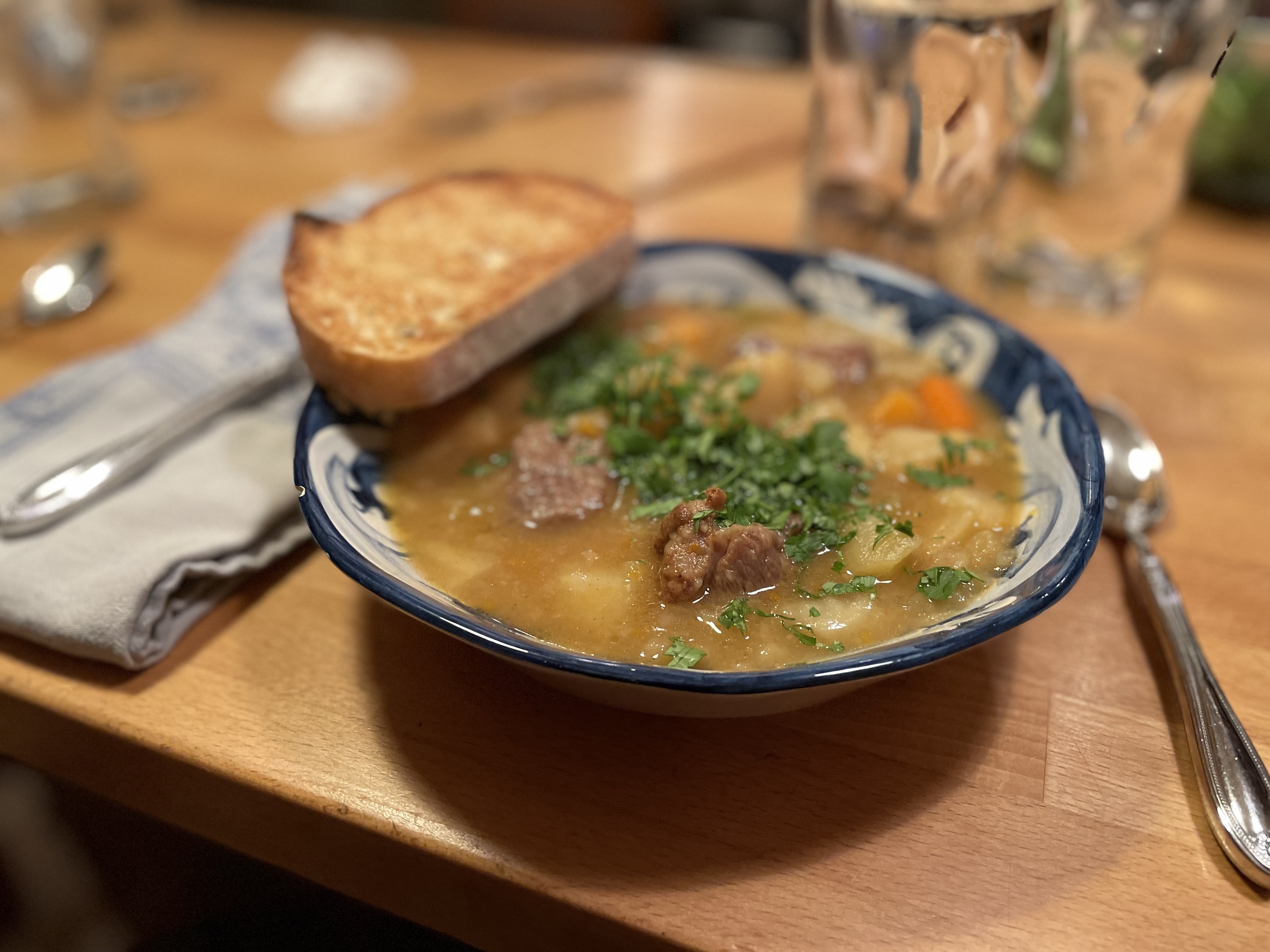 Bowl of soup with meat, noodles, and toasted bread on the side
