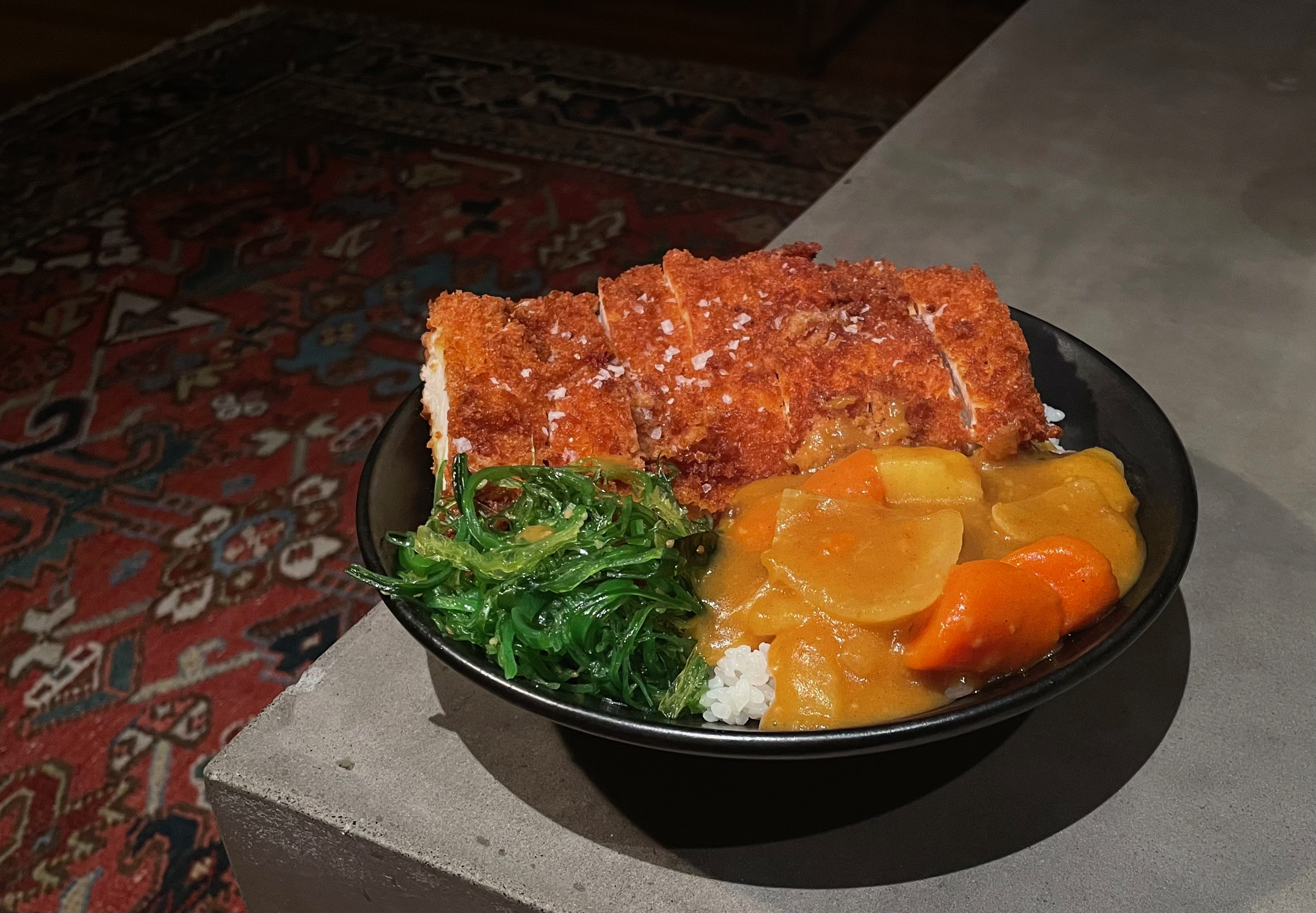Katsu curry bowl with breaded cutlet, Japanese curry, and seaweed salad