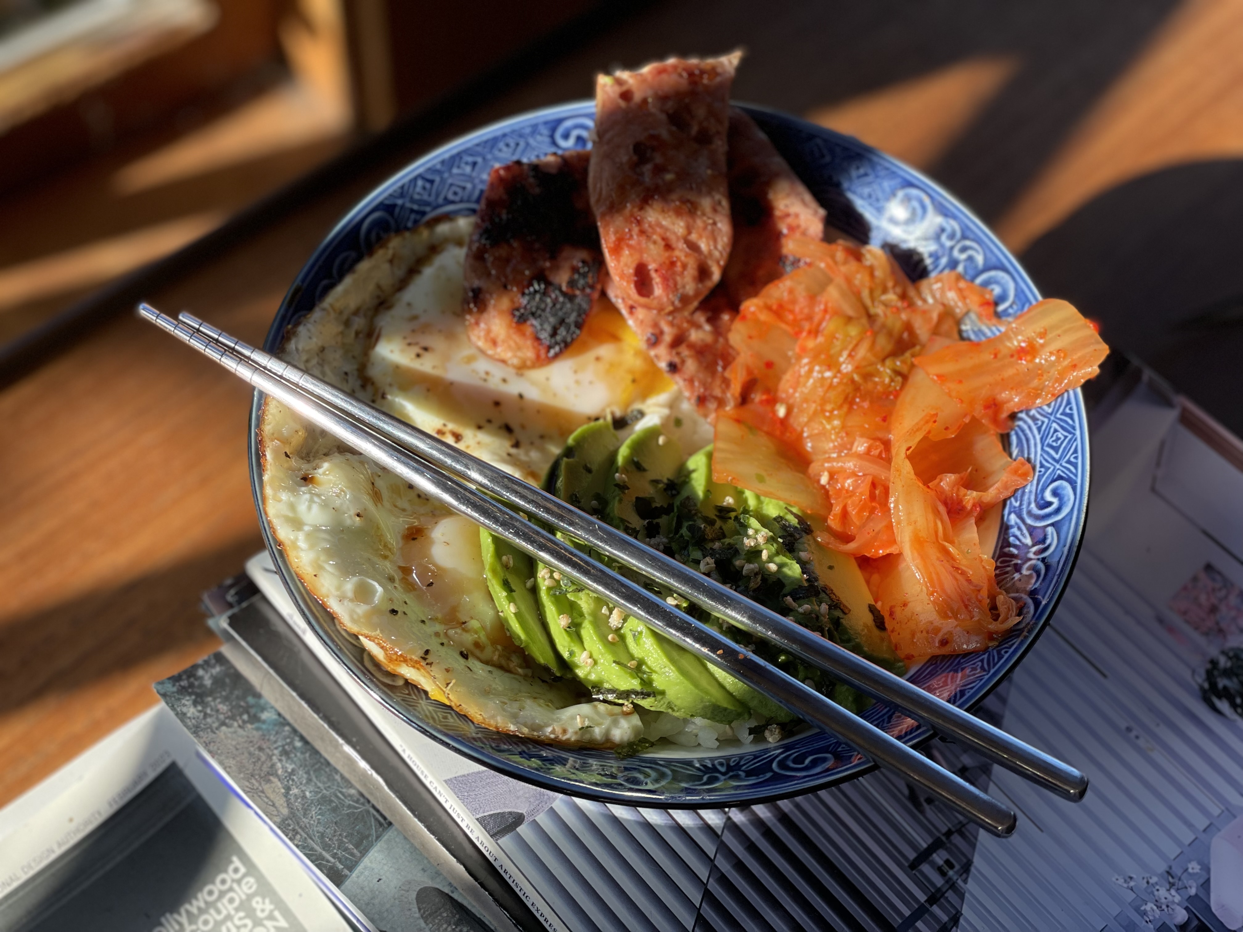 Rice bowl with fried egg, sliced avocado, kimchi, and spam with chopsticks