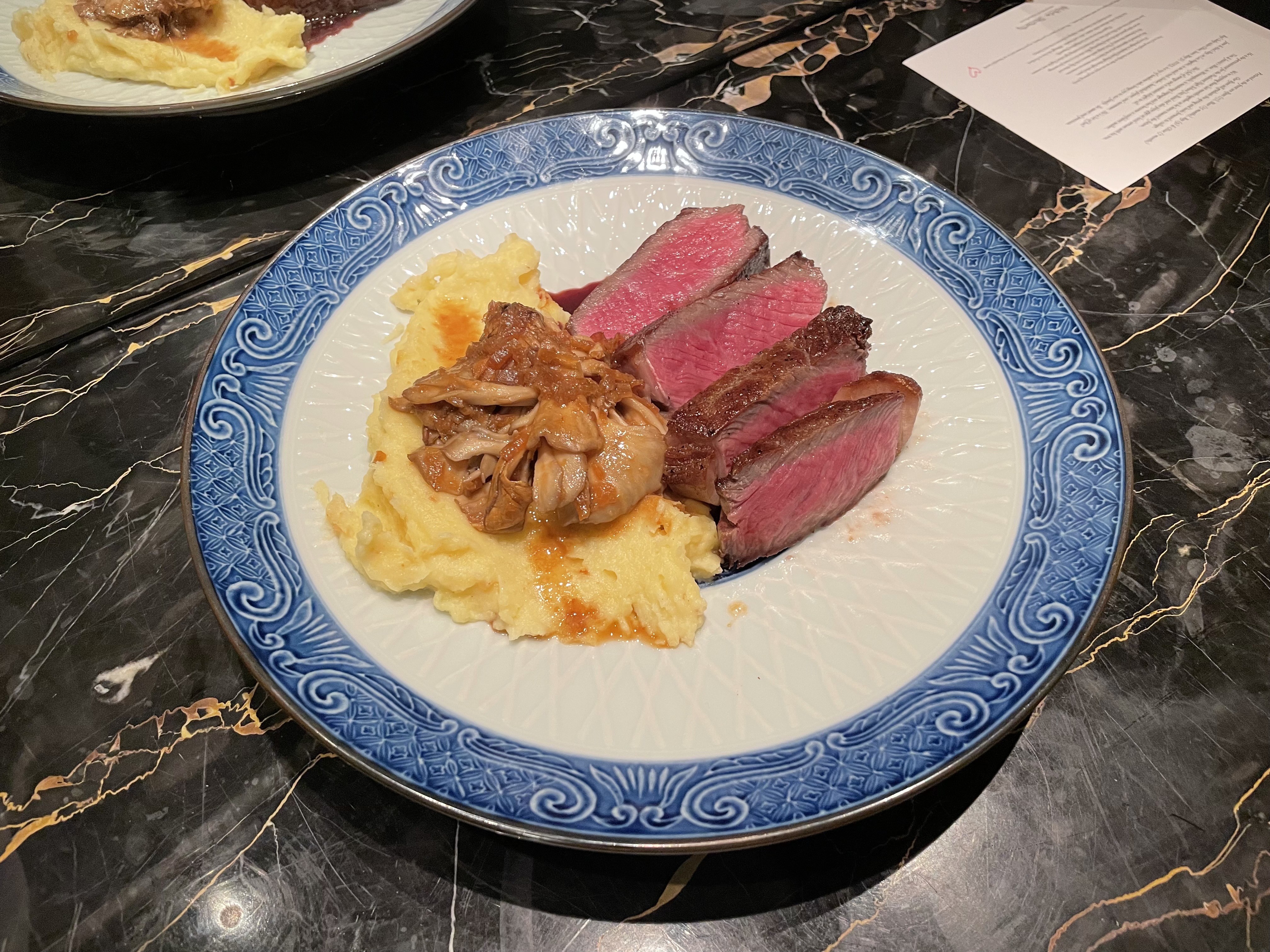 Sliced rare steak with mashed potatoes and caramelized onions on a decorative plate