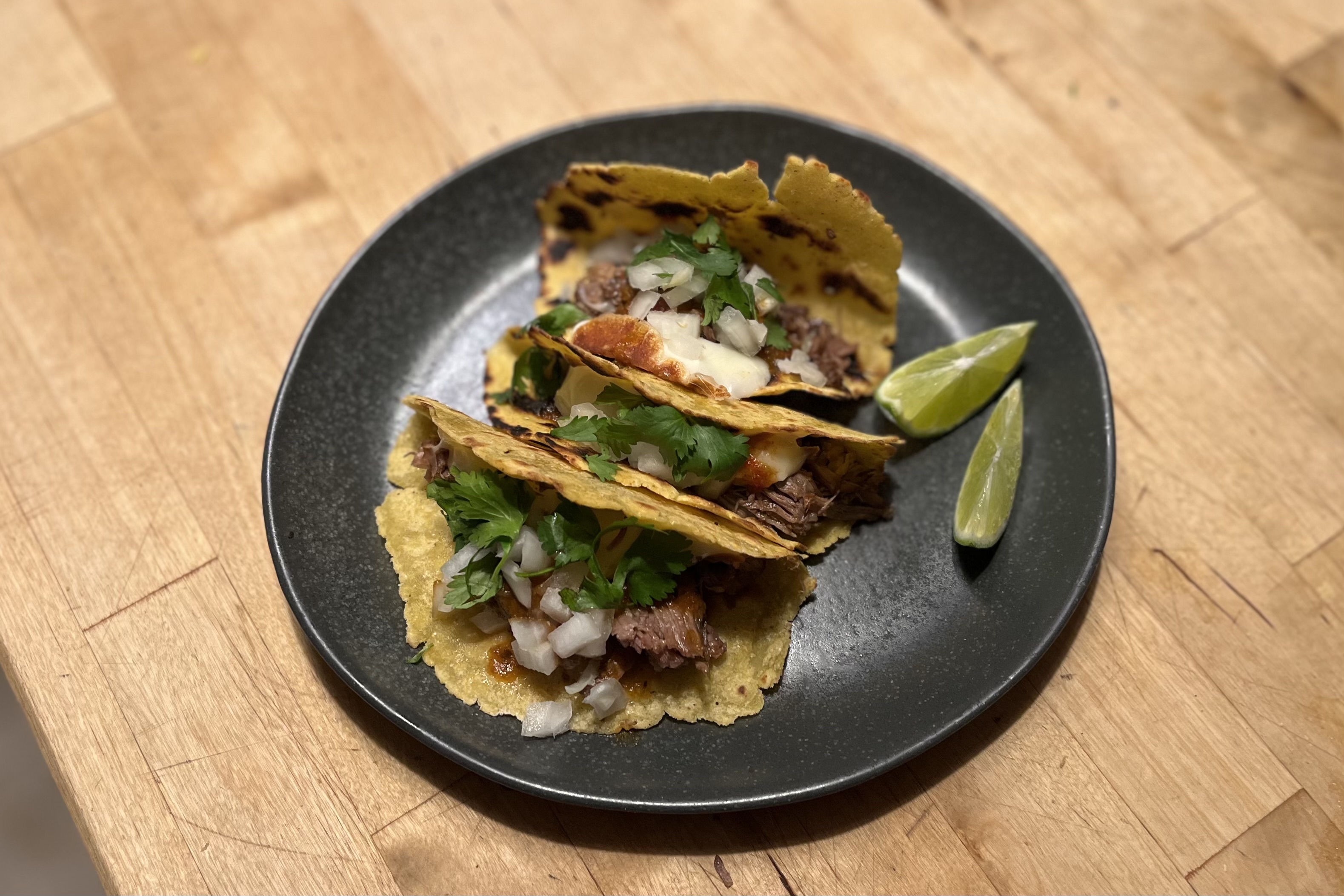 Three tacos with meat, onions, cilantro, and lime wedges