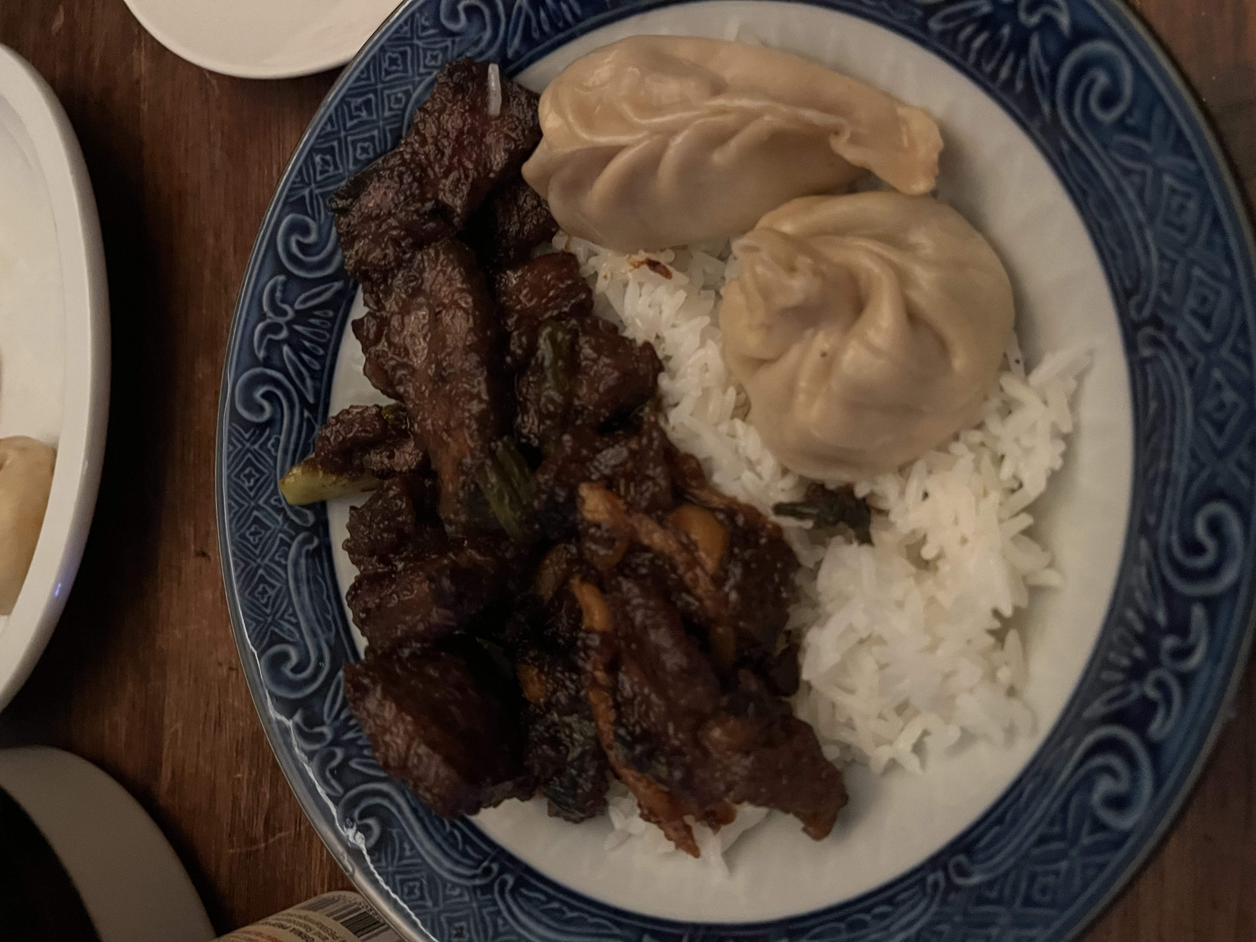 Braised beef with bok choy, steamed dumplings, and white rice on a blue and white plate