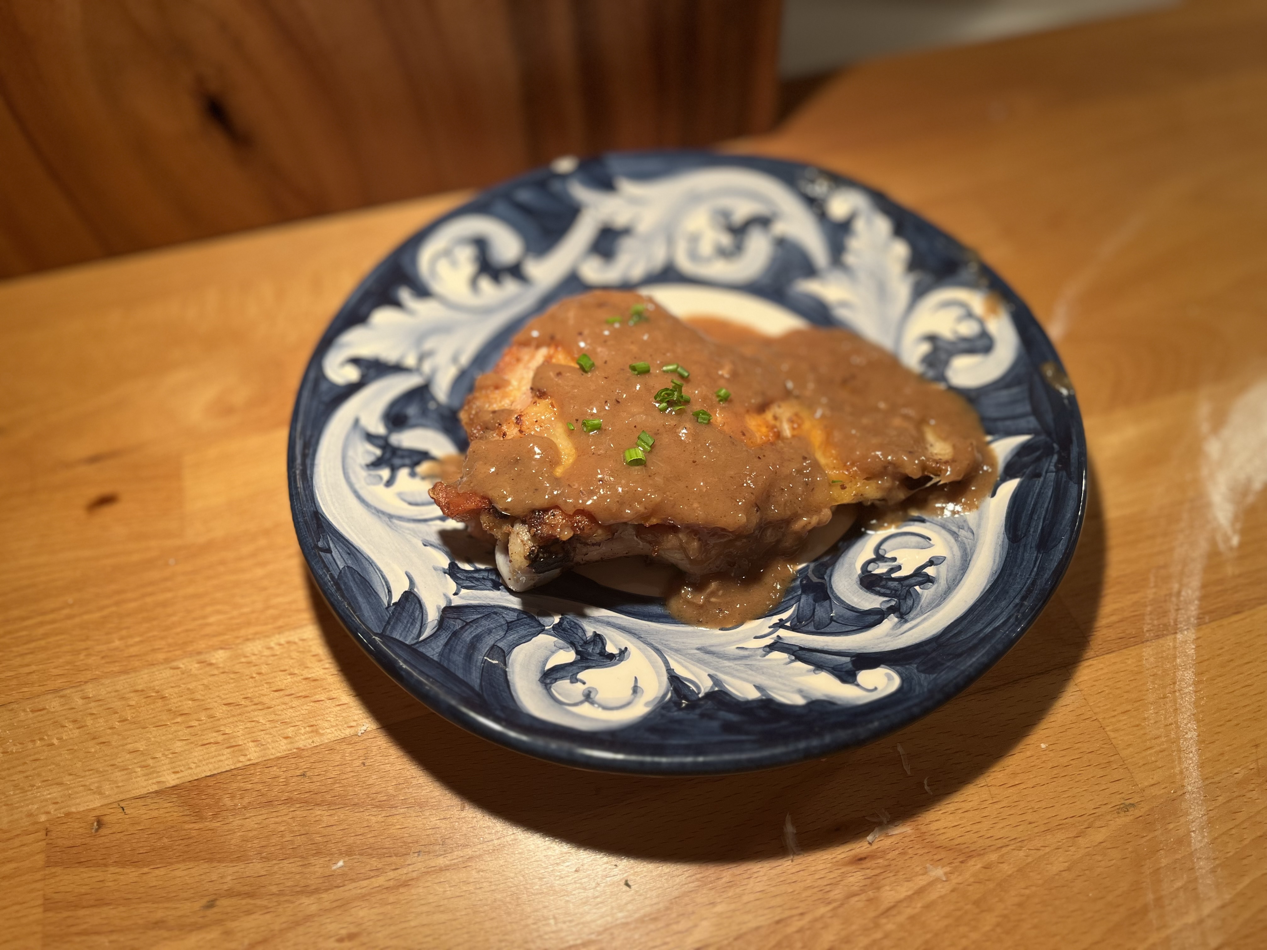 Pan-seared chicken with mushroom gravy and chives on a decorative blue and white plate