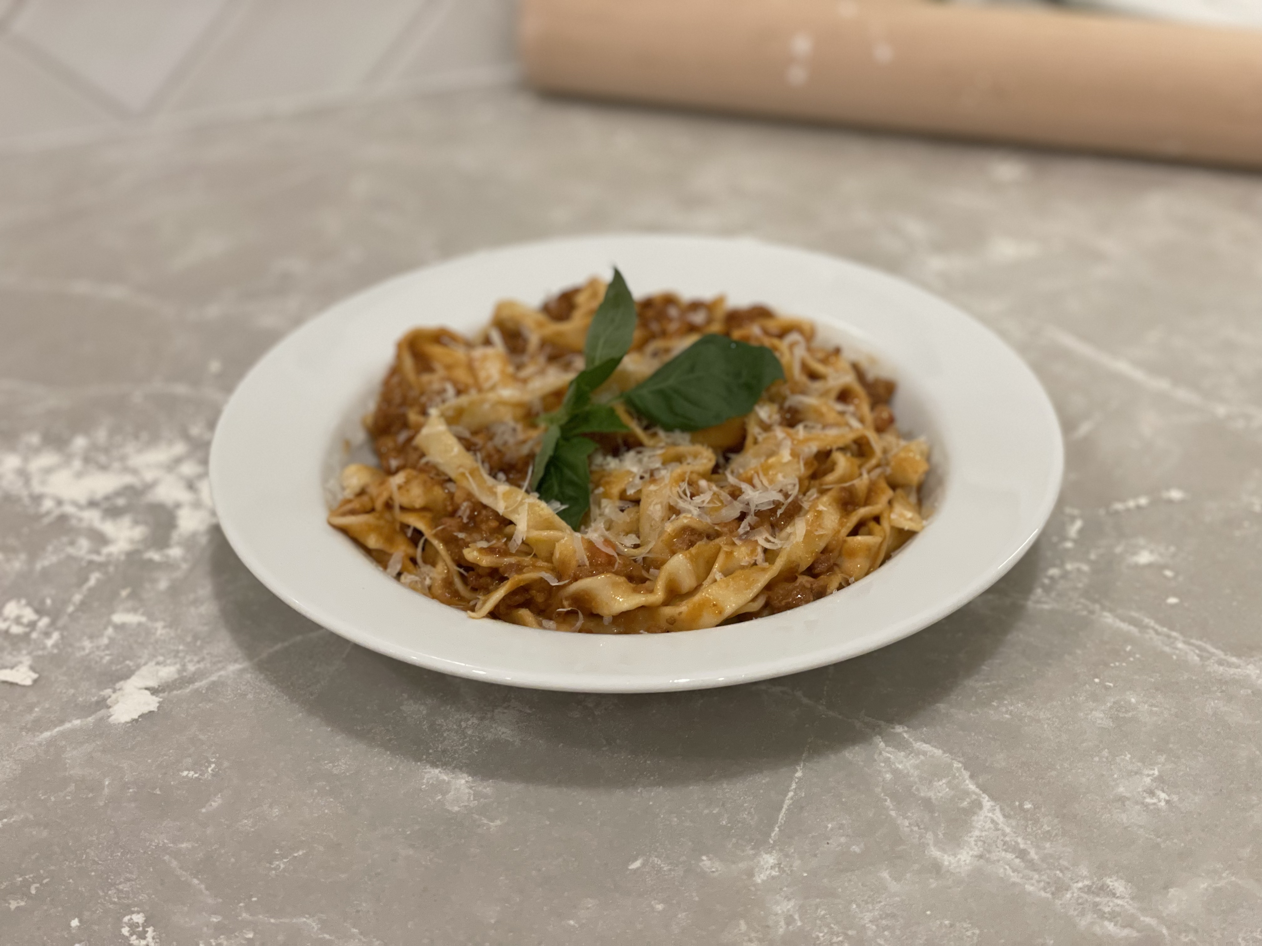 Fresh pappardelle with Bolognese sauce, grated Parmesan, and basil